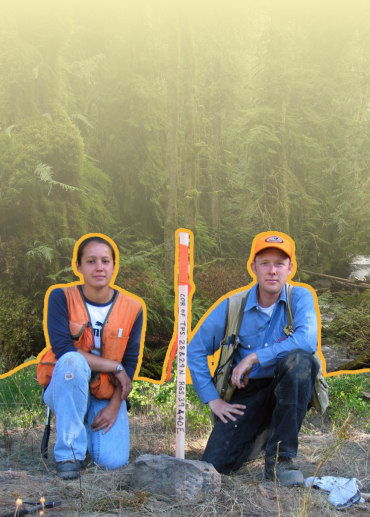 Two field workers kneeling in a forest, wearing orange vests, with a marked survey stake between them (site measurement).