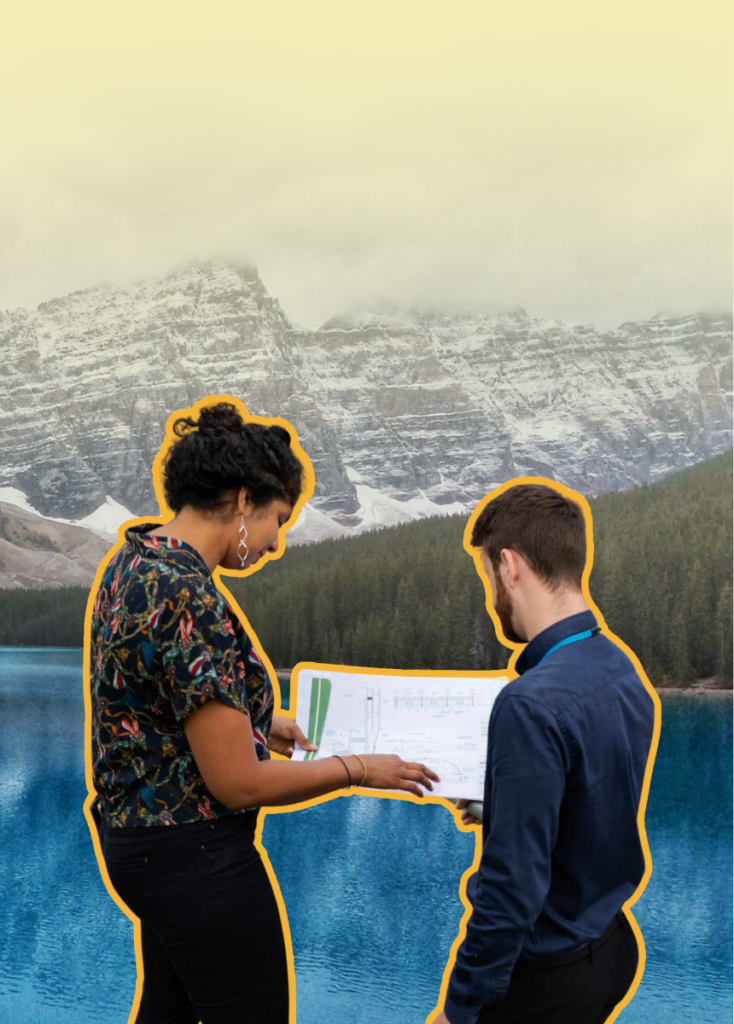 Two colleagues study a large document together outdoors by a turquoise lake with snowy mountains in the background.