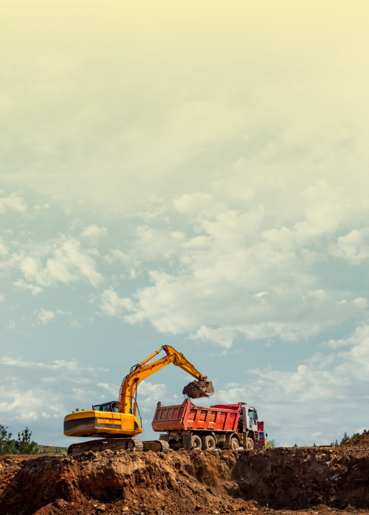 Yellow excavator loading dirt into a red dump truck on a construction site under a blue sky with clouds