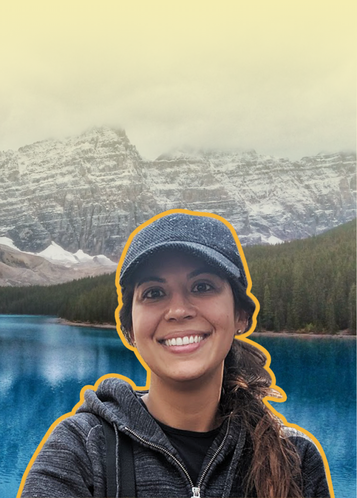 Smiling woman taking a selfie outdoors, with a turquoise lake and snow-capped mountains behind her.