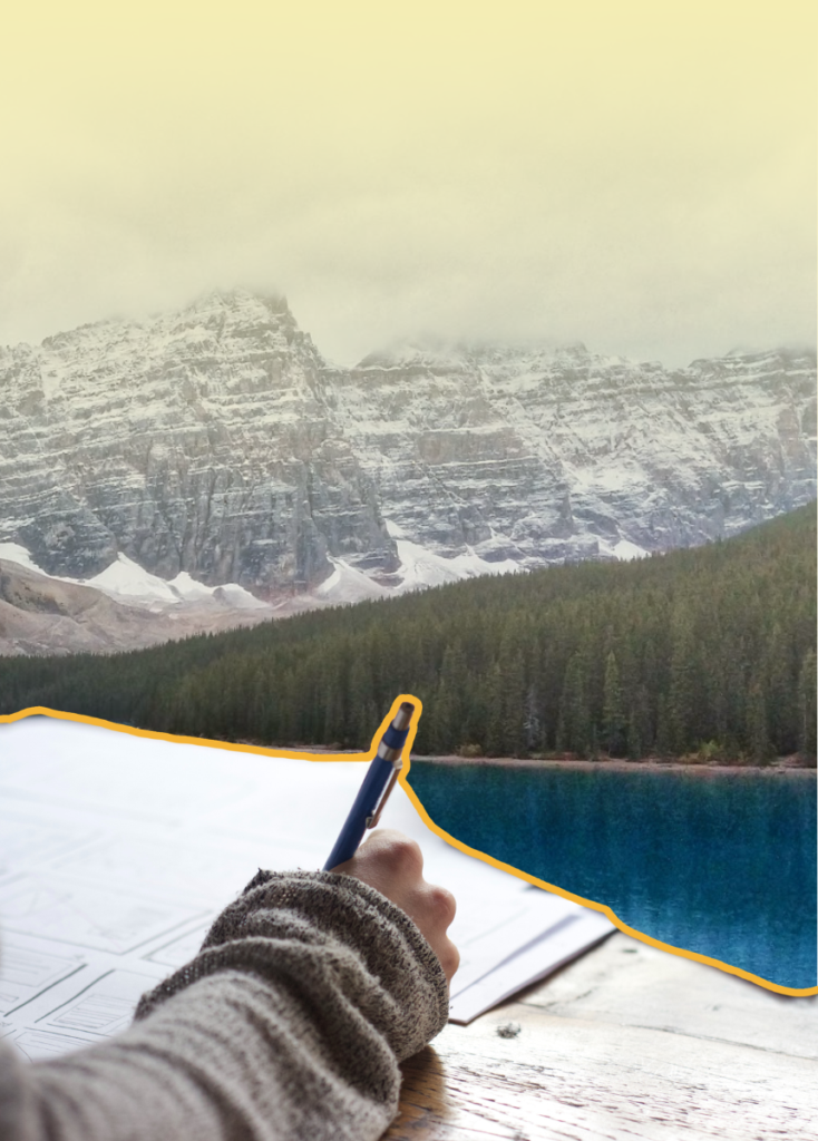 Person wearing a sweater writes on papers with a blue pen at a wooden table, mountains and a lake in the background