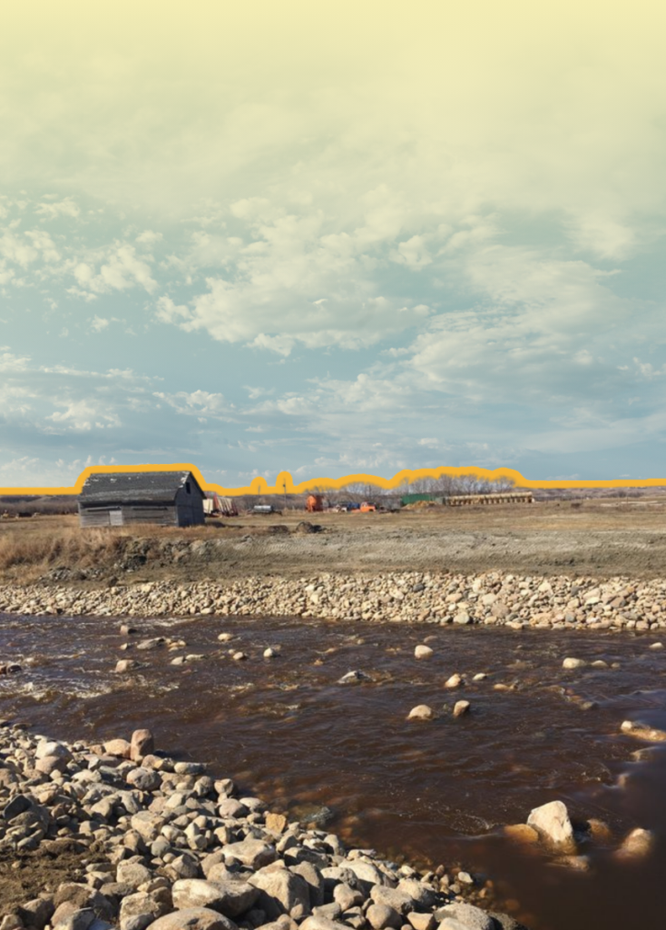 Riverside landscape with a rocky shore in the foreground, a small dark barn, and distant construction equipment on the horizon under a pale yellow sky.